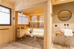 Ein modernes Badezimmer mit einer Holzbank, einer Duschkabine aus Glas und einem runden Spiegel.