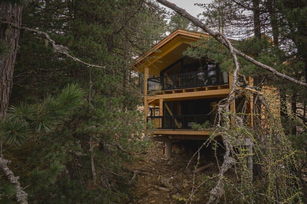 Kahden kerroksen korkuinen puinen mökki, jonka ympärillä on tiheä metsä.