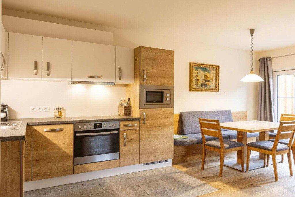 Une cuisine compacte dotée d’appareils électroménagers intégrés, un coin repas avec une table et des chaises, et une fenêtre avec des rideaux.