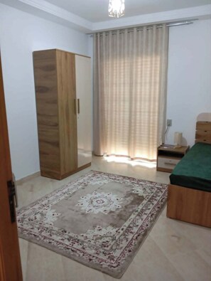 A bedroom with a wardrobe, a bed, a nightstand, and a large window with curtains. - A furnished apartment in Cité Ennasr, located on a private floor with no neighbors. (Ariana)