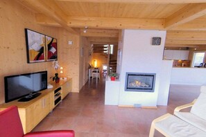 A modern living room with a flat-screen TV, a fireplace, and a red chair. - Cabin in Hohentauern with sauna (Hohentauern)