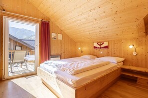Eine Holzhütte mit einem Einzelbett, einer Bank und Blick auf Berge durch eine Schiebetür.