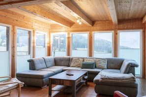 A cozy cabin interior with a sectional sofa, a small table, and large windows offering a view of the outdoors. - Cabin in Hohentauern with sauna (Hohentauern)