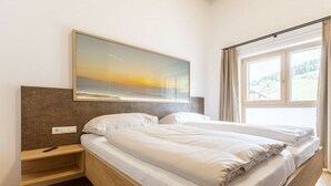 Quarto com cama, mesa de cabeceira, quadro na parede e janela com cortinas.