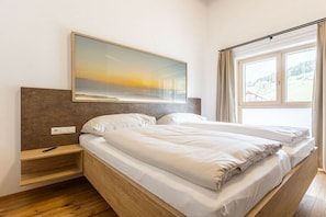 Ein Schlafzimmer mit einem Bett, einem Nachttisch, einem Wandbild und einem Fenster mit Vorhängen.