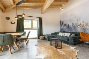 Ein Zimmer mit Holzboden, einem grünen Sofa, einem Esstisch mit Stühlen und einem Kuhfellteppich.