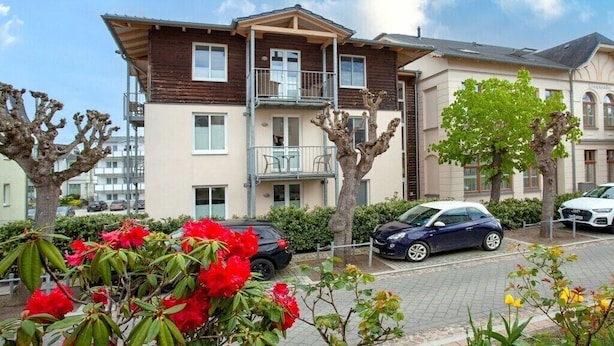 Un edifici d'apartaments de diverses plantes amb balcons, cotxes aparcats i plantes en flor.