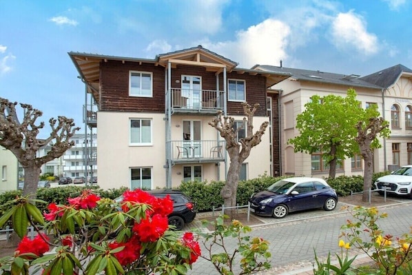 A multi-story residential building with balconies, parked cars, and flowering plants. - Apartment building Linquenda 12 (Ahlbeck (Seebad))