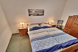A bedroom with a bed, two bedside lamps, a chair, a wooden wardrobe, and a wall-mounted picture. - Holiday apartments Lindenstraße (Ahlbeck (Seebad))