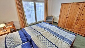 Habitació d'hotel amb un llit, una cadira, un armari de fusta i una finestra amb cortines.
