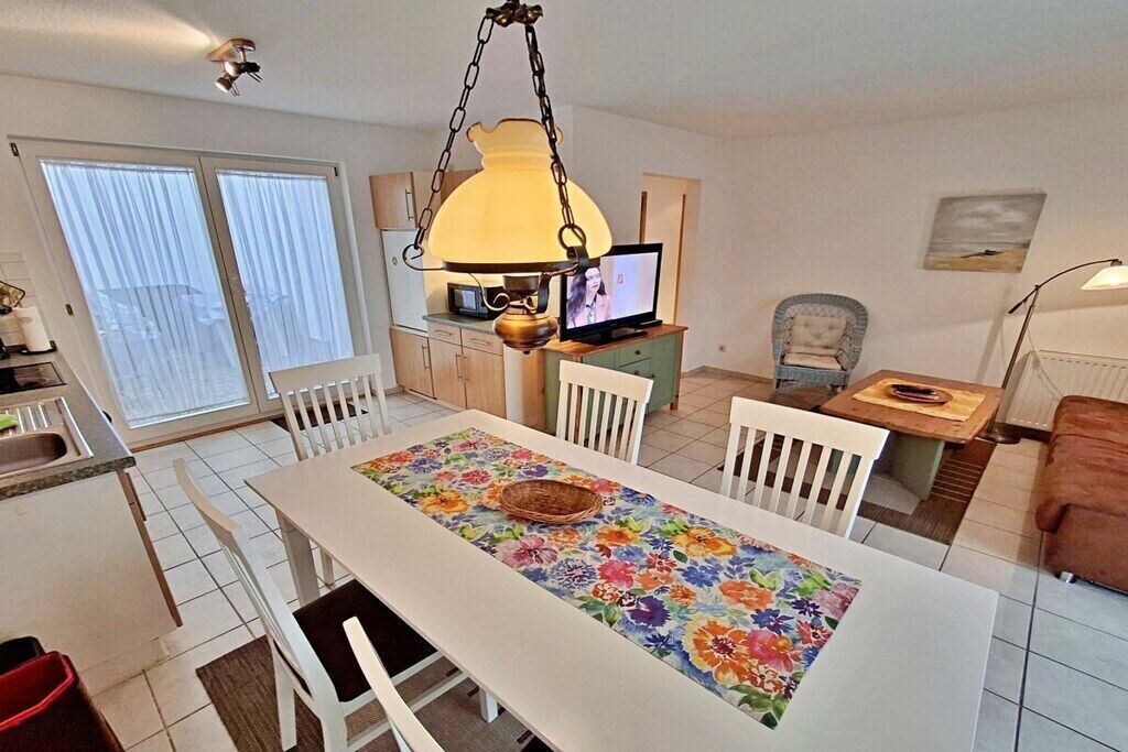 A dining area with a table set for four, a television, and a chair with a cushion.