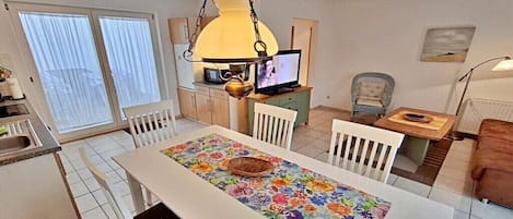 A dining area with a table set for four, a television, and a chair with a cushion.