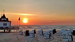 Una platja amb un edifici blanc i un moll, i diverses cadires blanques amb números.