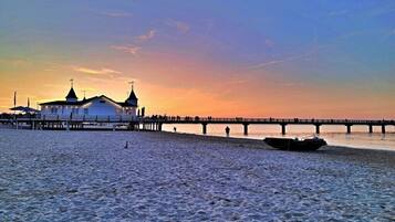 A beach with a pier extending into the water, a boat, and a building with a cross on top.