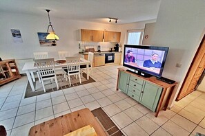 A compact living space with a dining area, kitchenette, and a television displaying a program. - Holiday apartments Lindenstraße (Ahlbeck (Seebad))