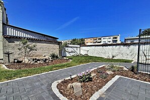 A courtyard with a paved walkway, a stone wall, and a small garden area with flowers and rocks. - Holiday apartments Lindenstraße (Ahlbeck (Seebad))