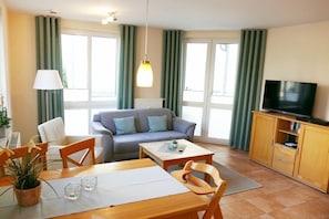 Una sala de estar con sofá, mesa de comedor, sillas, televisor y aparador.