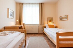 Ein Zimmer mit zwei Holzbetten, einem Schreibtisch, einem Stuhl, einer Heizung und einem Fenster mit Vorhängen.