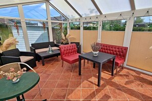 A covered patio area with outdoor furniture, including sofas and a table, and a view of the surrounding area through large windows. - Holiday apartment Seahorse (Ahlbeck (Seebad))