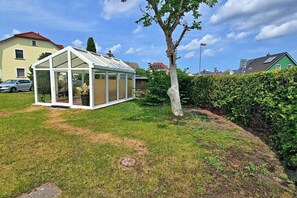 A glass greenhouse structure in a residential area with a lawn and a hedge. - Holiday apartment Seahorse (Ahlbeck (Seebad))