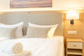 Une chambre d’hôtel avec un lit, des oreillers, une table de chevet, une lampe et un tableau représentant une scène de plage.