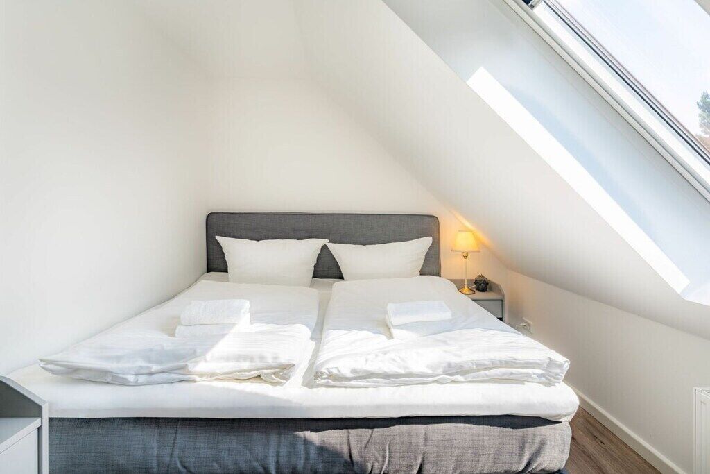 A single bed with a grey headboard in a room with a sloped ceiling and a skylight.
