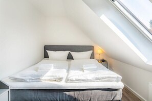 Ein Einzelbett mit grauem Kopfteil in einem Zimmer mit schräger Decke und Dachfenster.