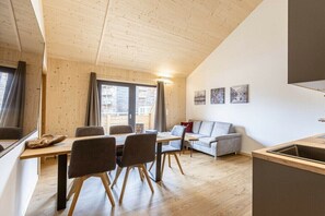 A modern interior with a wooden ceiling, a dining area with chairs and a table, a sofa, and a kitchen area with a sink. - Apartment with 1 bedroom (St. Georgen am Kreischberg)