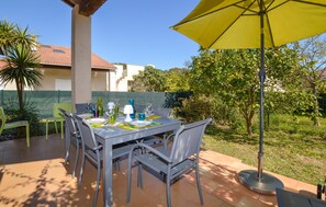 Eine Terrasse im Freien mit Esstisch und Stühlen, beschattet durch einen gelben Sonnenschirm.