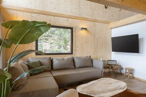 A modern living room with a sectional sofa, a coffee table, and a large window with a view of trees. - Superior Chalet # 21 with Sauna & Hot Tub (Turrach)