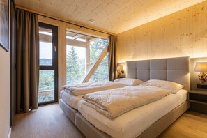 A bedroom with a large bed, a window with curtains, and a view of trees. - Superior Chalet # 21 with Sauna & Hot Tub (Turrach)