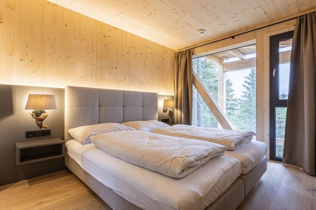 A bedroom with two beds, wooden walls, a window with curtains, and a nightstand with a lamp.