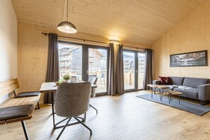 Ein Zimmer mit Holzwänden und -böden, einer Couch, einem Esstisch mit Stühlen und Blick durch große Fenster.