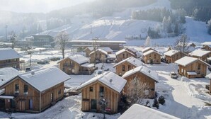 Um conjunto de cabanas de madeira com telhados cobertos de neve, com a paisagem nevada de uma montanha ao fundo.