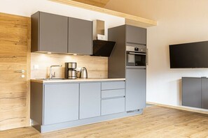 Eine moderne Küche mit grauen Schränken, einem eingebauten Backofen und einem an der Wand befestigten Flachbildfernseher.