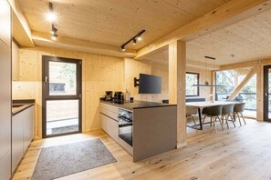 A modern kitchen with wooden walls, a central island, and a dining area with chairs. - Superior Chalet #15 with Sauna & Hot Tub (Turrach)
