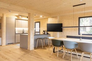 A modern interior with a wooden floor, a kitchen area, and a dining space with chairs and a table. - Superior Chalet #15 with Sauna & Hot Tub (Turrach)