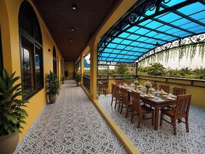 A covered outdoor dining area with a patterned floor, potted plants, and a table set for dining. - Tam Coc Amana Boutique Hotel (Nam Hoa Lu)