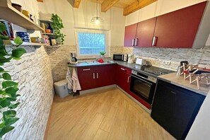 Una cocina con pared de piedra, techo de madera, armarios rojos y horno empotrado.