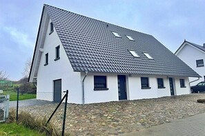 Une maison moderne, blanche, avec un toit à forte pente, des fondations en pierre et une clôture en métal.
