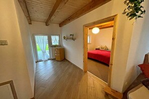 Huoneessa on puinen katto, punaisella peitteellä varustettu sänky, puinen lipasto ja ovi, joka johtaa toiseen huoneeseen.