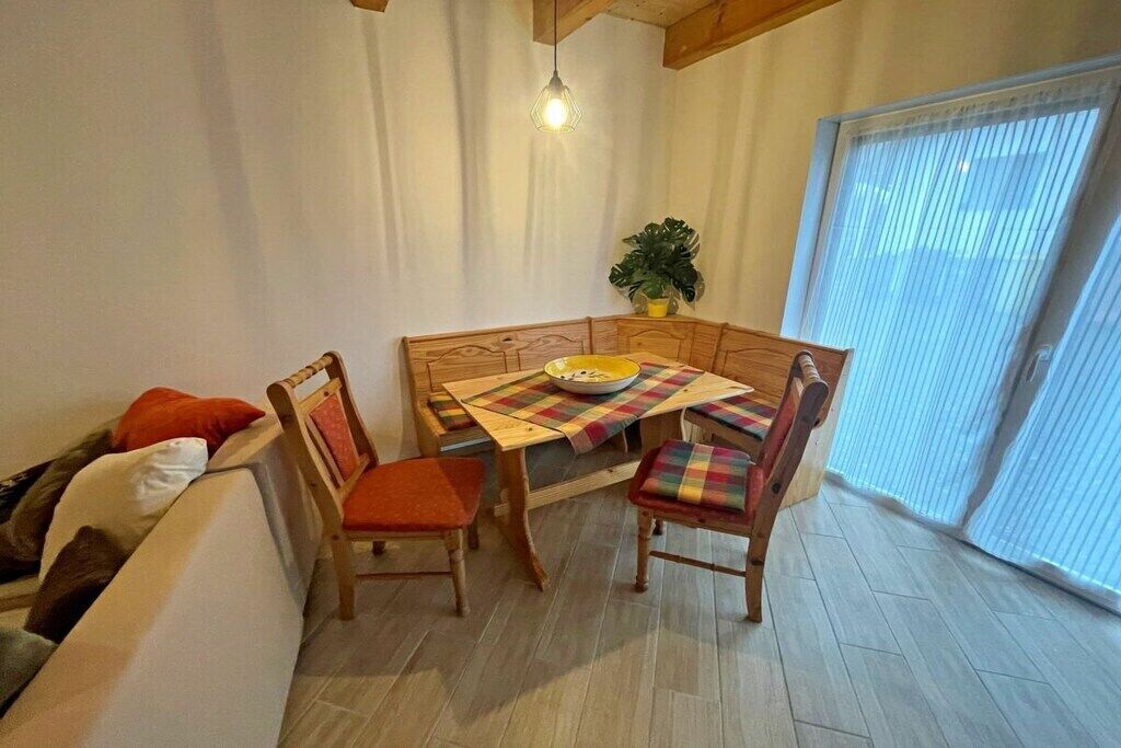 Zona de dinar amb taula i caires de fusta, una planta en test i una finestra amb persianes.