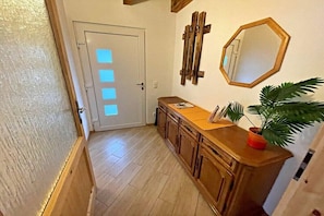 A hallway with a wooden cabinet, a potted plant, and a door with a light panel. - Holiday apartment with 1 bedroom (Zirchow)