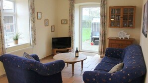 Ein Wohnzimmer mit einer Couch, einem Fernseher, einem kleinen Tisch mit Flasche und Gläsern sowie einem Schrank.