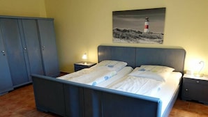 A bedroom with a bed, two bedside tables, a nightstand, a wardrobe, and a painting of a lighthouse. - Holiday apartment with 1 bedroom (Hasselberg)