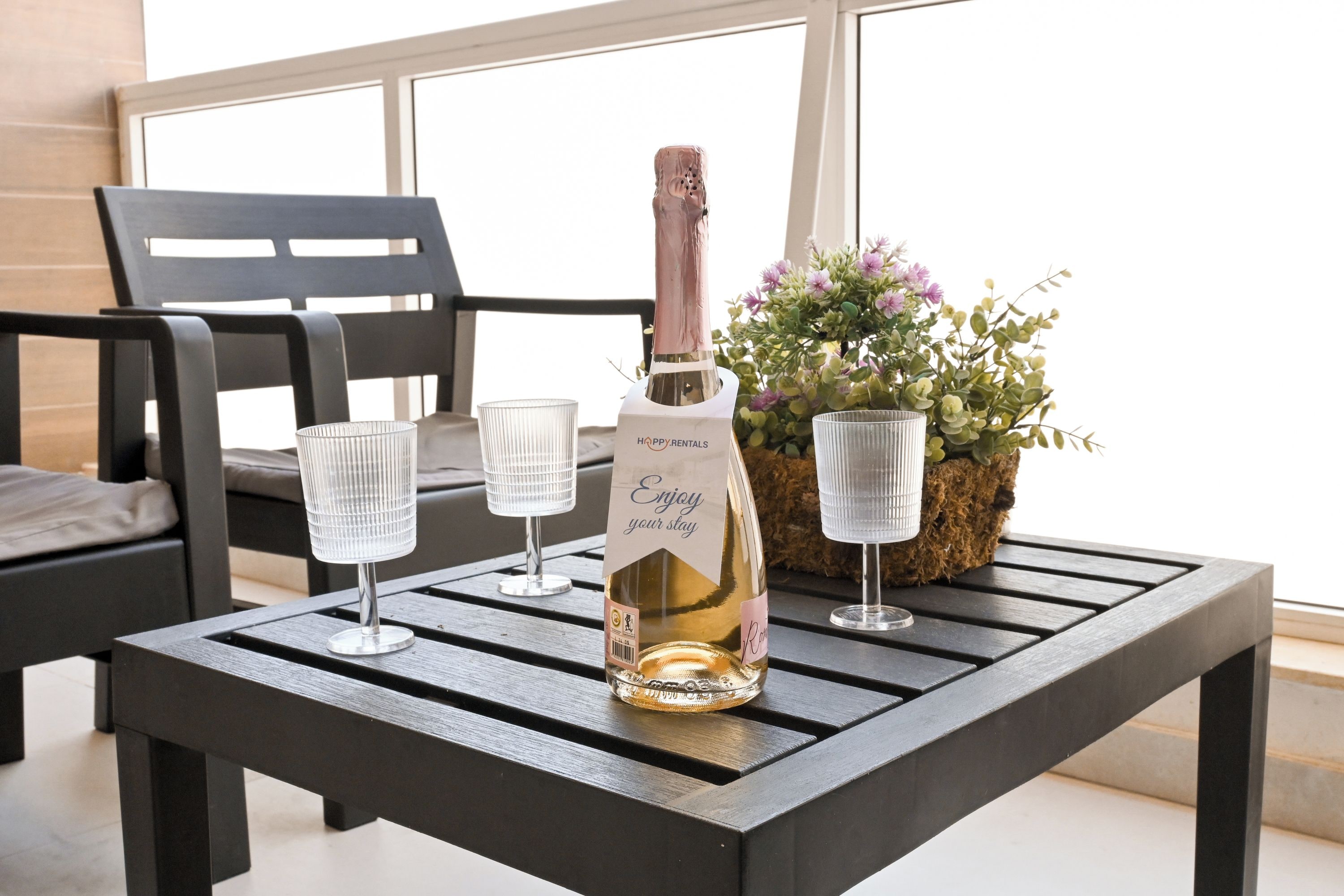 A bottle of champagne on a table with two glasses, a potted plant, and a chair.