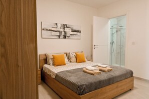 A bedroom with a wooden bed, a glass shower enclosure, and a wall-mounted abstract artwork. - Comfort & Modern Sea-view 3 bdr Apart (St. Paul's Bay)
