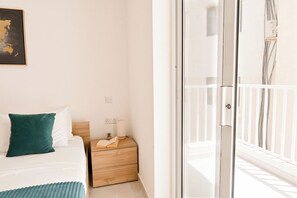 Een slaapkamer met een bed, nachtkastje, stopcontact aan de muur en een raam.