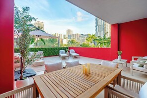A modern outdoor patio with a wooden table, white chairs, and a red wall. - Unique Terrace in Midtown Pool (Miami)