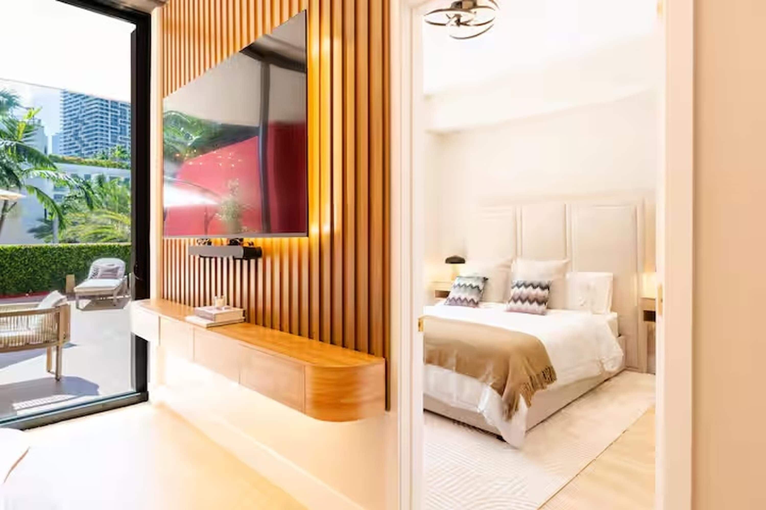 A modern bedroom with a large bed, a built-in TV, and a view of a cityscape.